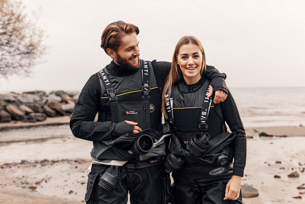 Man and woman in scuba gear on a beach.